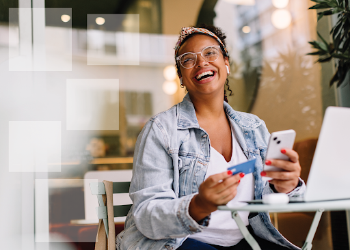 Smiling woman holding a credit card and smartphone at a cafe, symbolizing understanding credit reports and financial planning