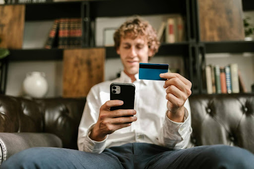 A man looking at his phone while holding his card, utilizing online banking benefits